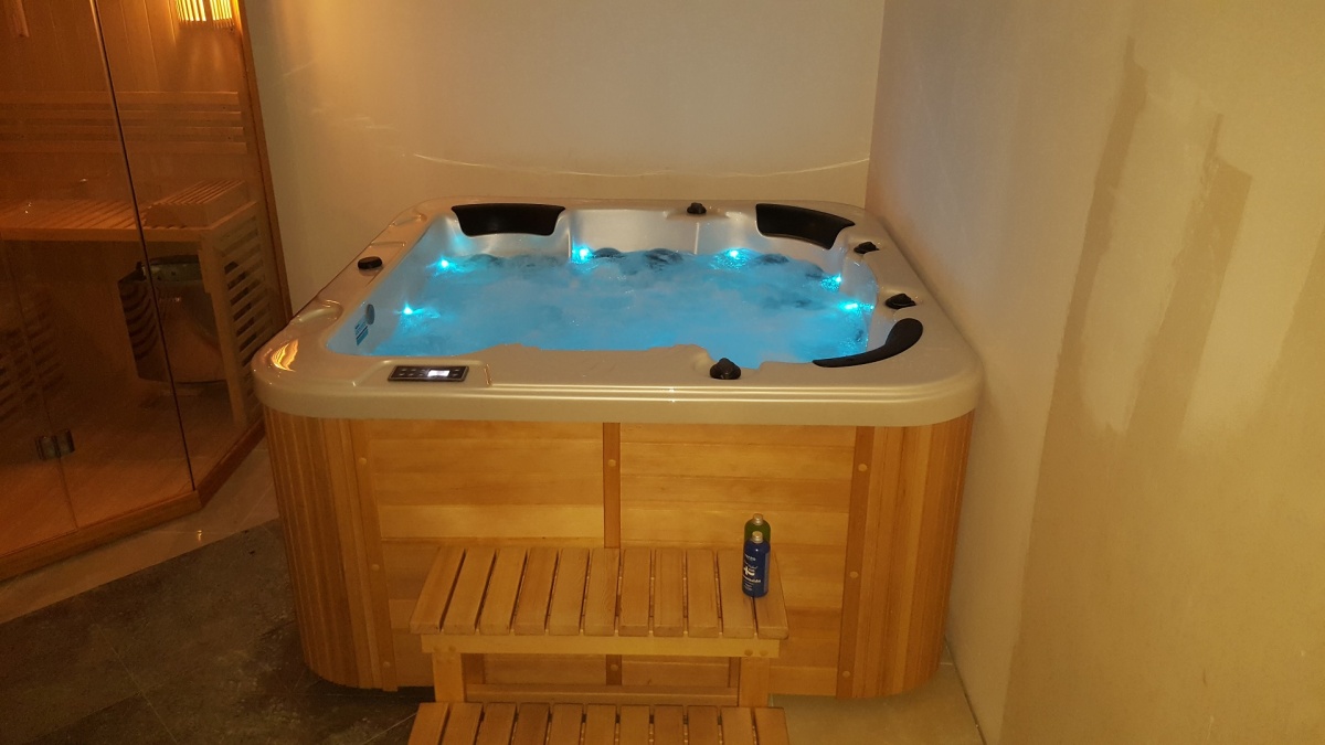 health by fun indoor wooden hot tub with blue underwater lights and built-in headrests in a cozy room.