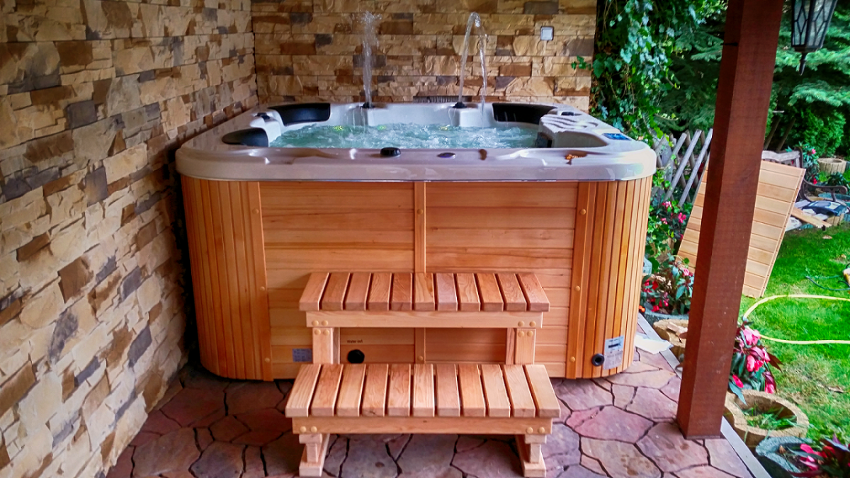 » Health By Fun health by fun wooden outdoor hot tub with bubbling water on a stone-paved patio, next to a stone wall and wooden steps/stairs.